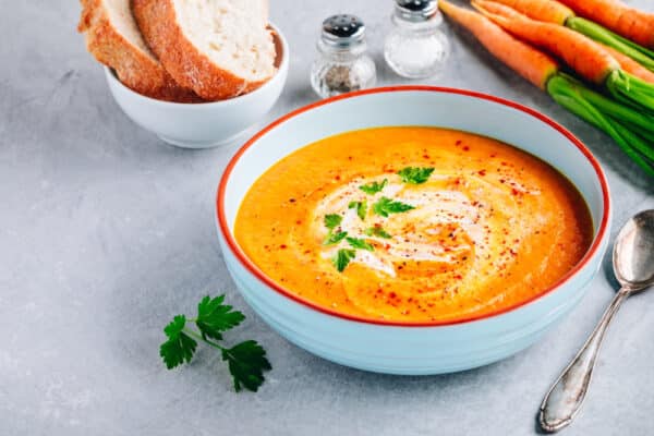 Cremige Steckrüben-Möhren-Suppe mit Kokosmilch, dekoriert mit gerösteten Kürbiskernen und frischen Kräutern.